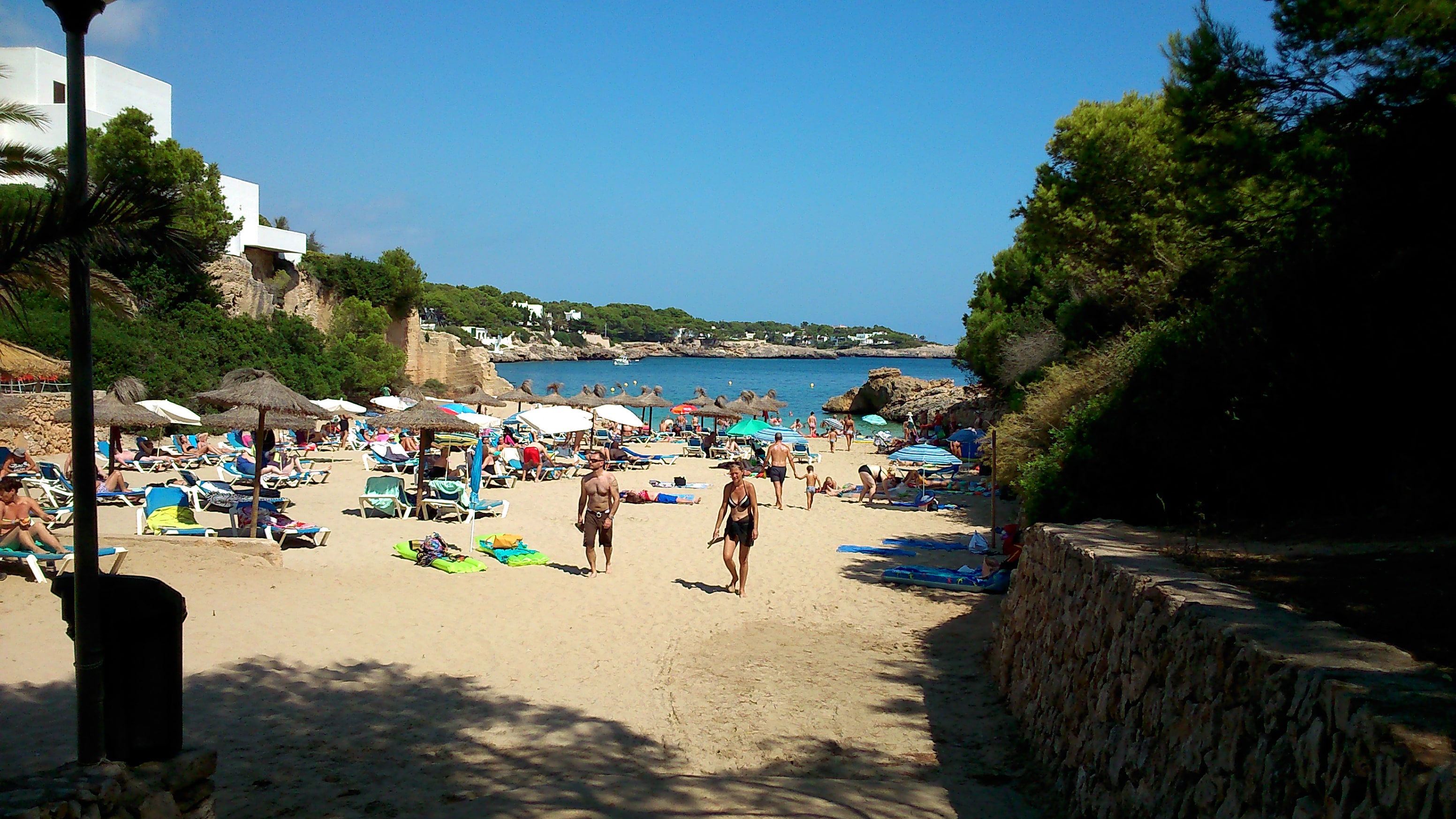 Sandy beach with bathers, parasols and blue water in Cala d’Or