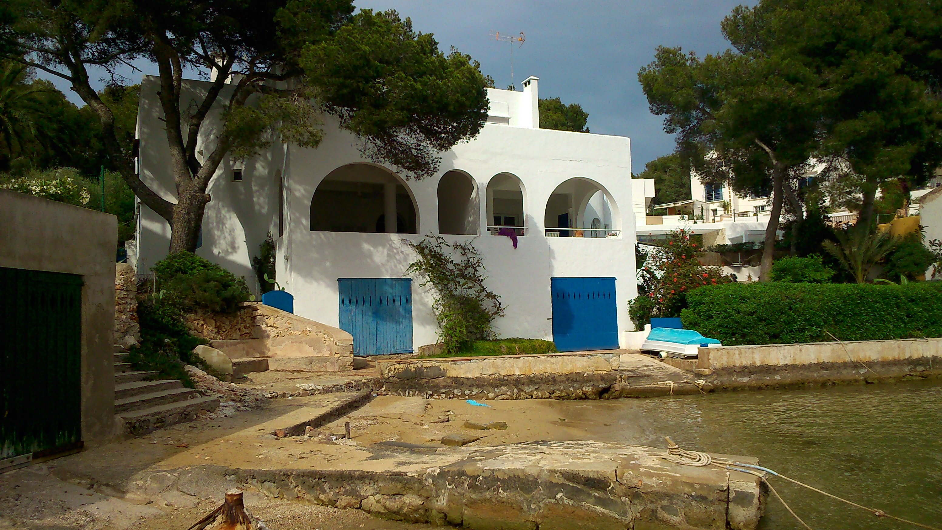 White house with arches and blue doors beside the water in Cala d’Or