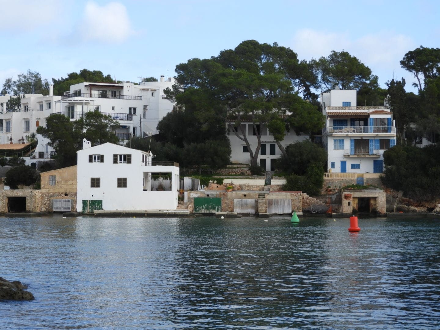 White houses and pine trees overlooking the water with coloured buoys in Cala d’Or